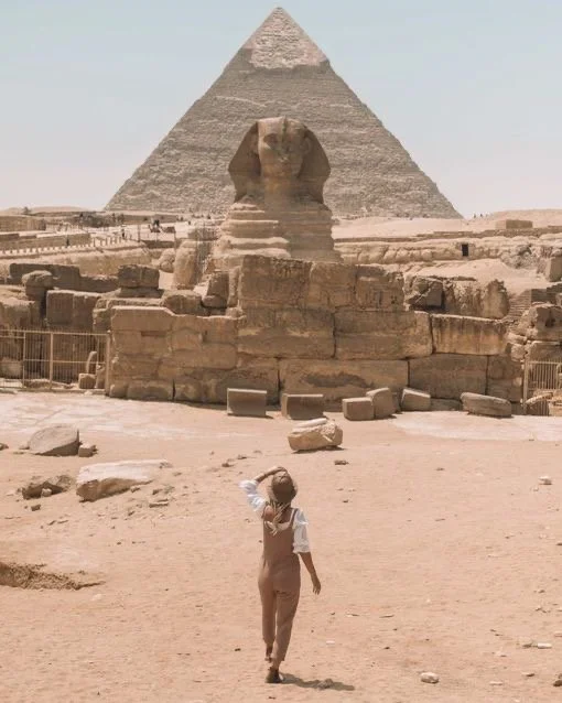 A young boy in light-colored clothing points towards the Great Sphinx and pyramid in Giza, Egypt.
