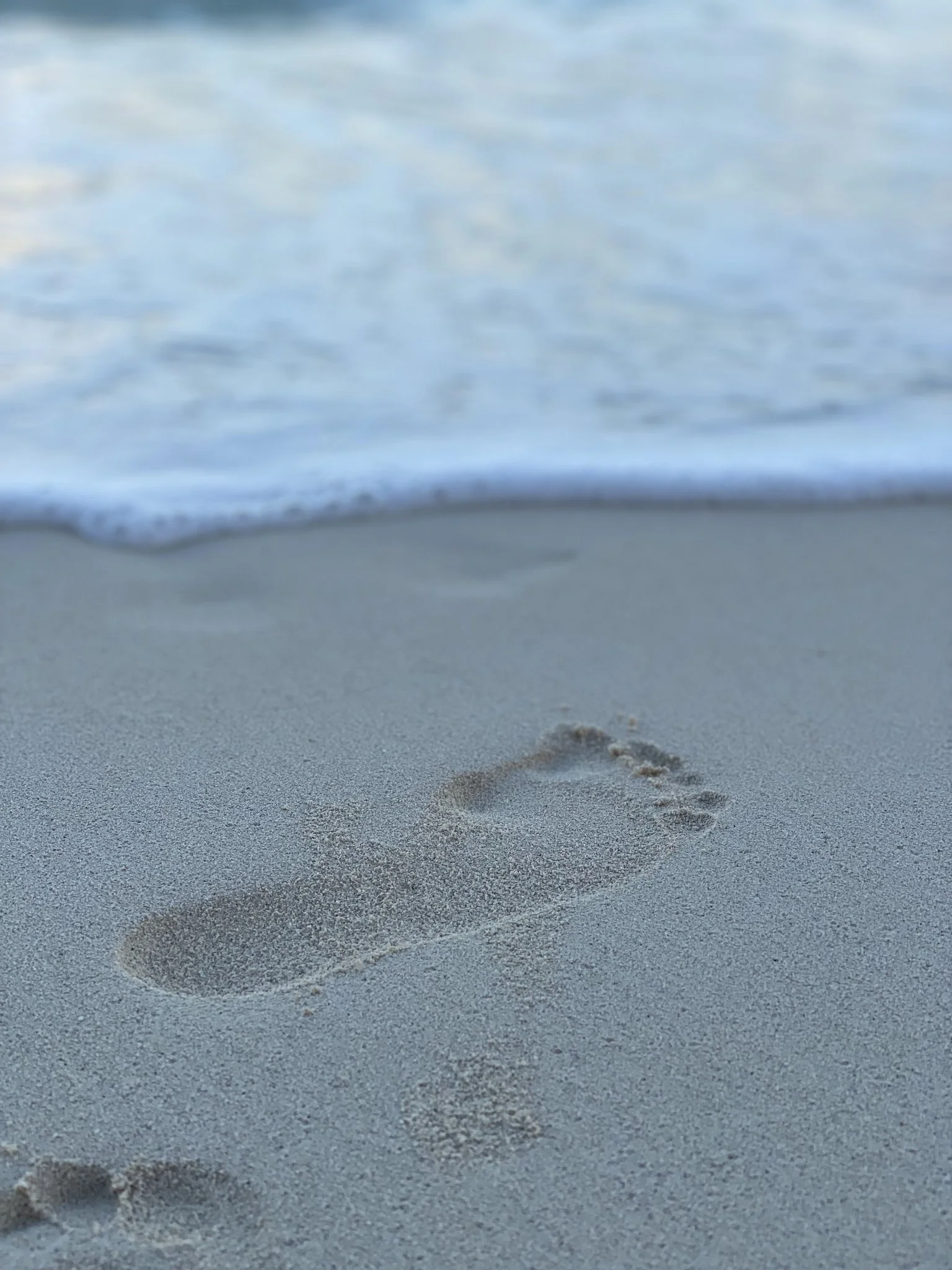 Footprints in the sand near the shoreline with gentle waves in the background.