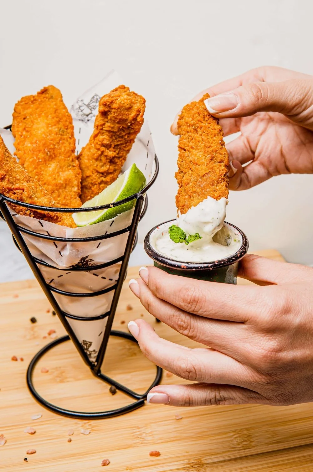 A person dipping a chicken tenders nto a small cup of dipping sauce