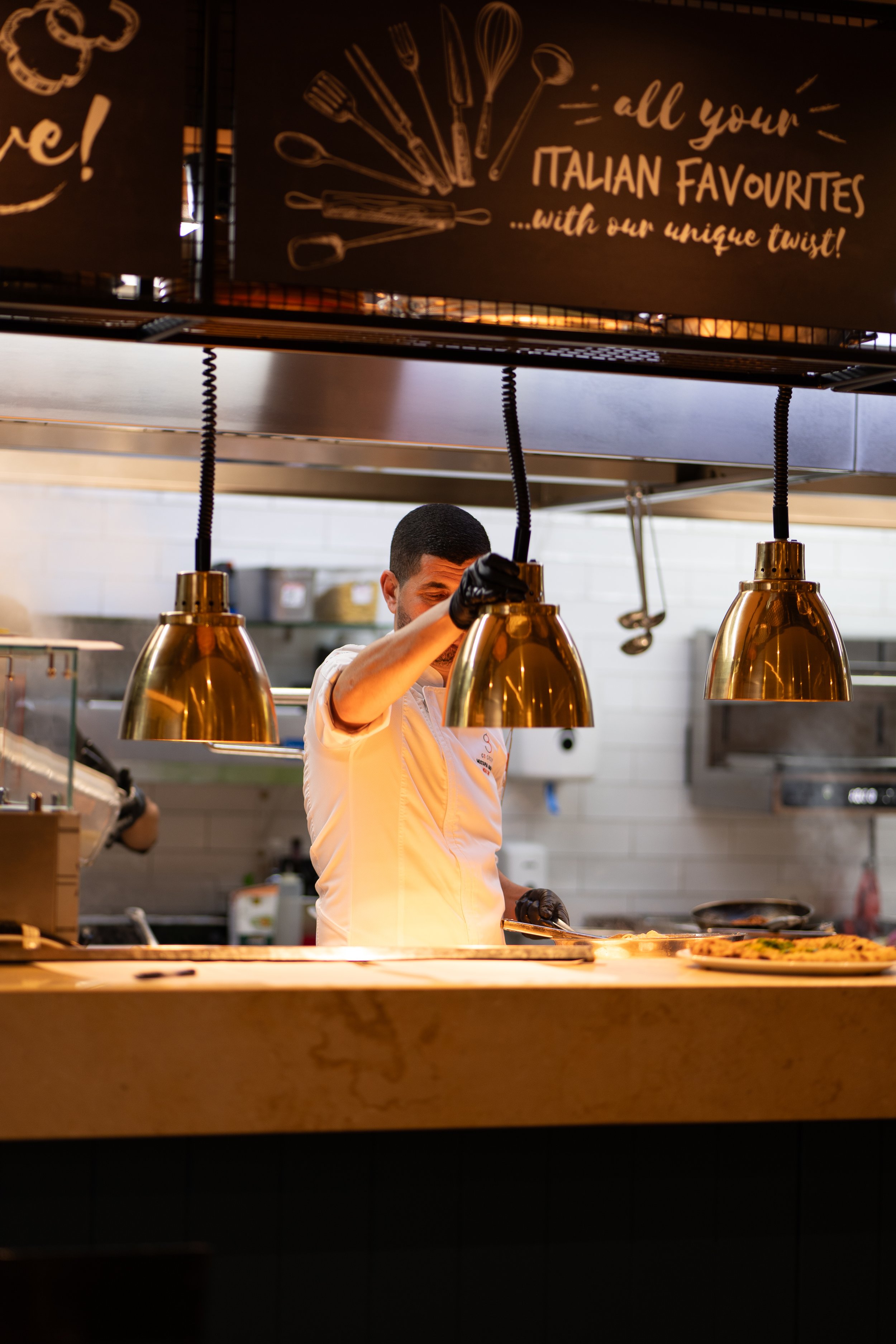 Hospitality photography capturing a chef preparing dishes in an open kitchen, highlighting the energy and professionalism of a restaurant in Malta.