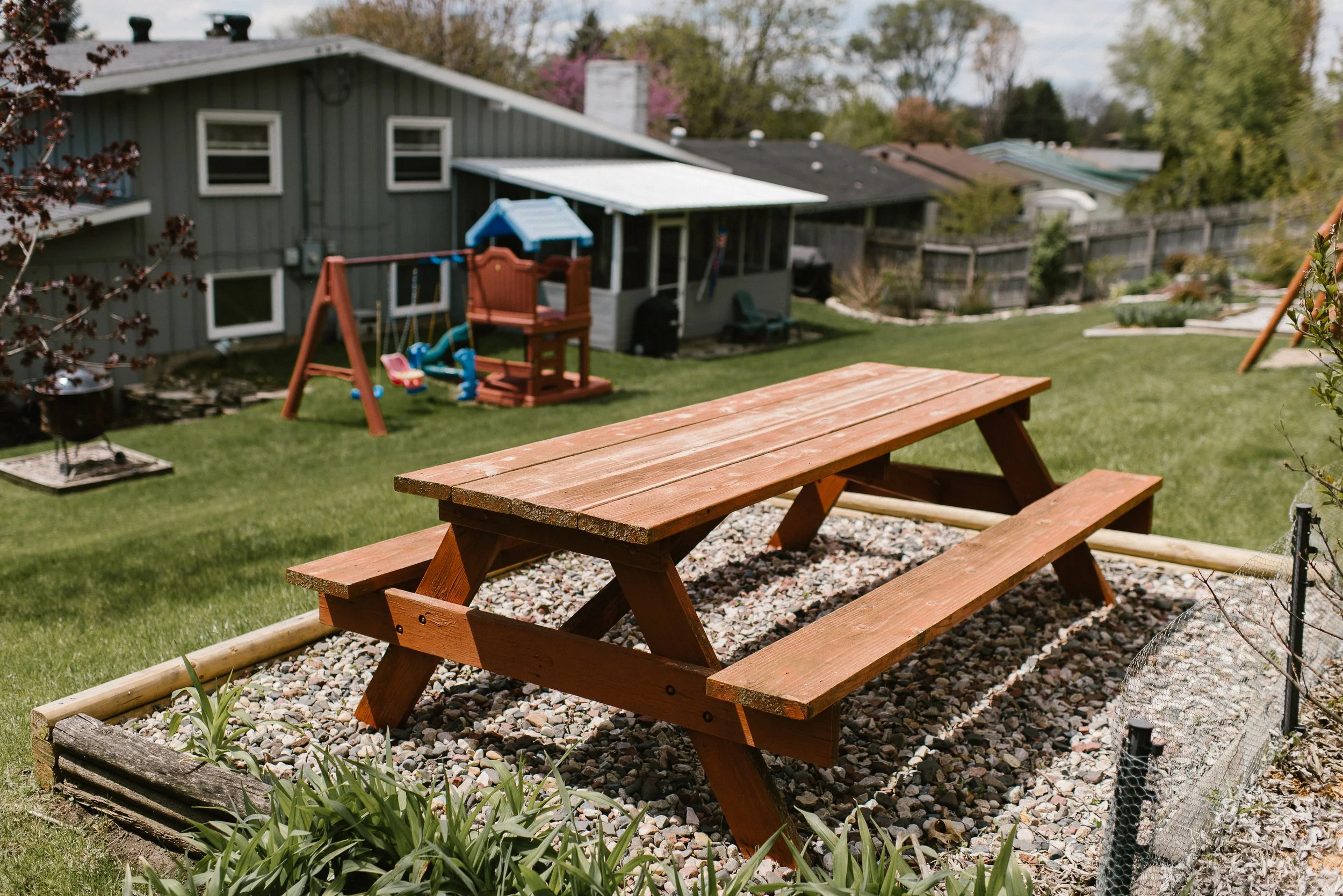 Backyard with wooden picnic table, grass, and children's playset with slide and swings.