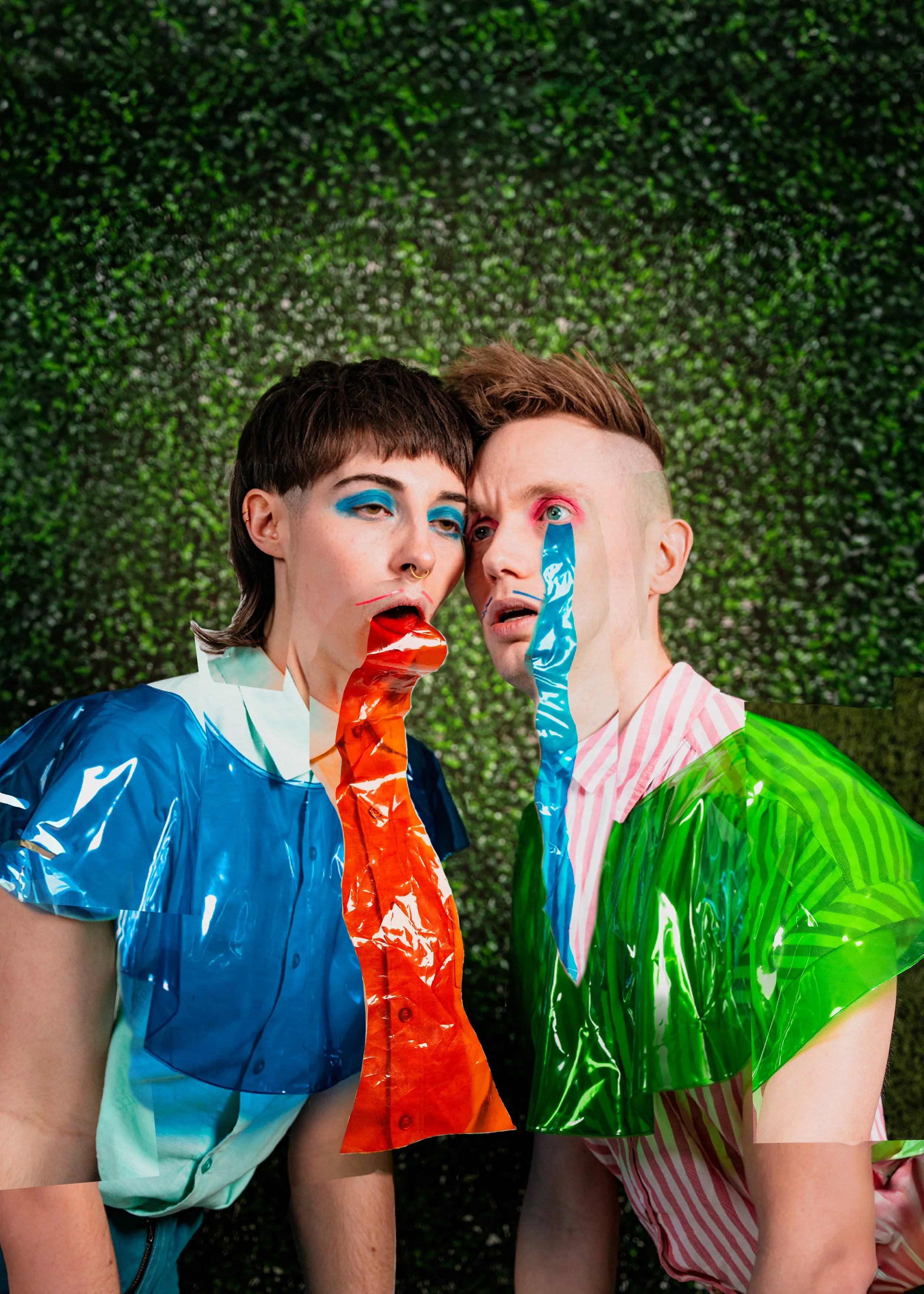 Two people with colorful face paint and shiny, brightly colored clothing are leaning close to each other against a green, leafy background.