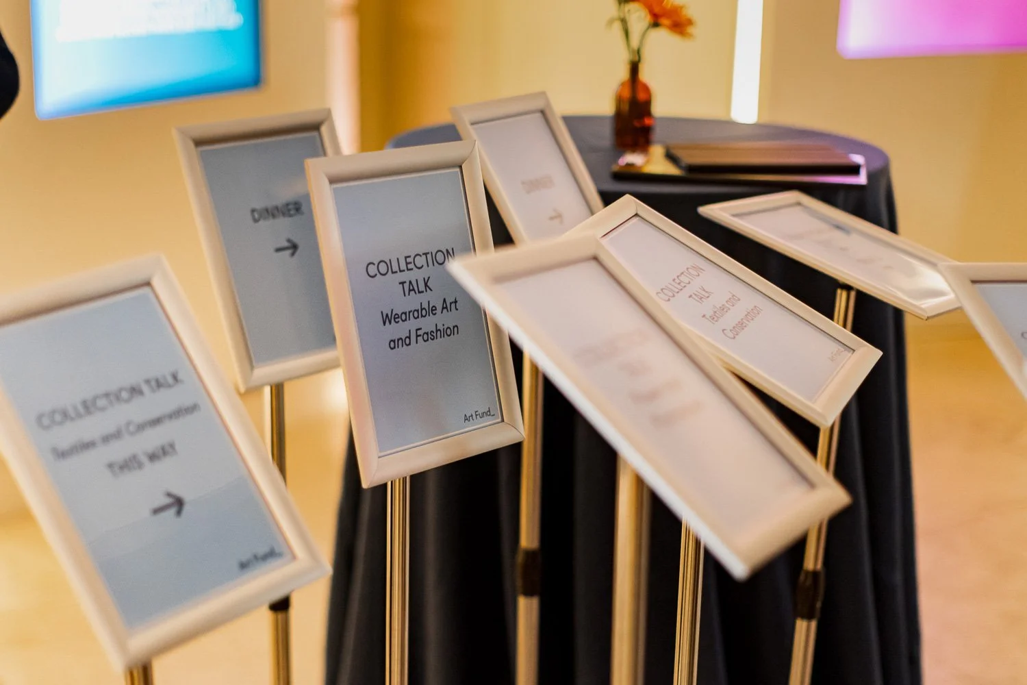 Several framed signs on gold stands with text about wearable art and fashion collection talk at an event.