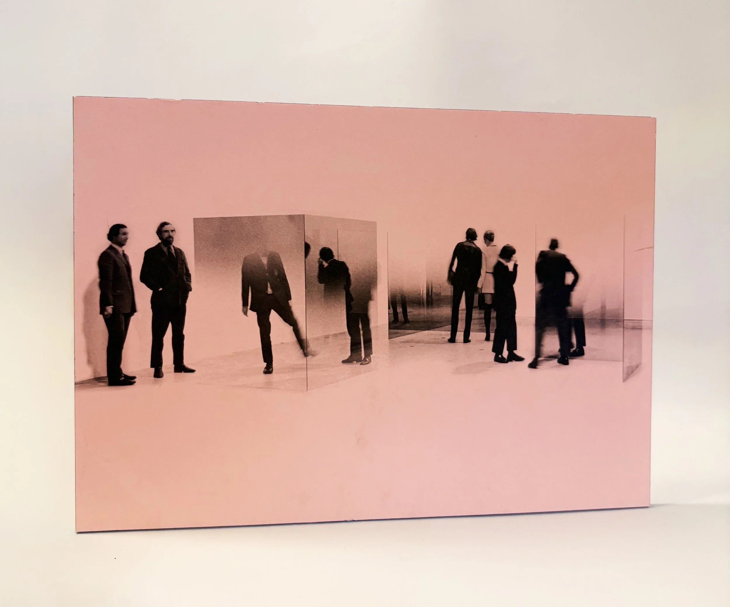 People standing and walking in an indoor space with a large pink wall or structure in the background.