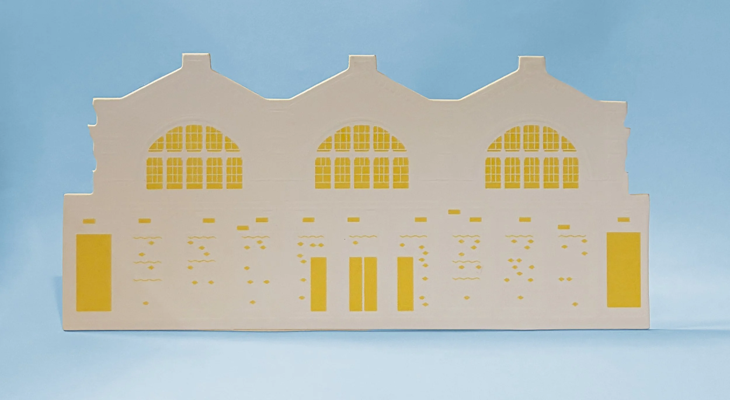 A paper cutout of a building with arched windows and decorative elements, placed against a light blue background.