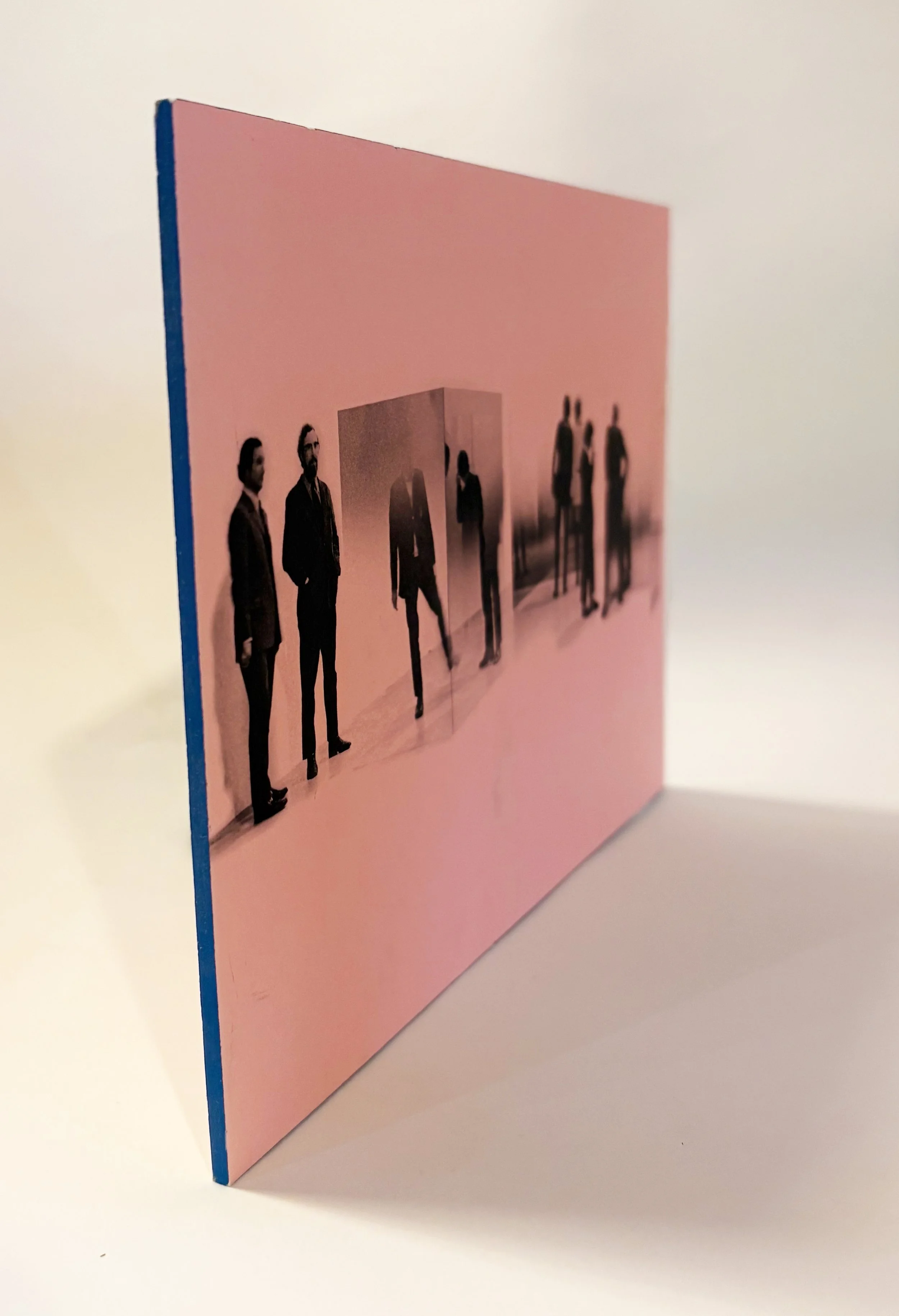 A pink greeting card with a printed photo of six men dressed in black suits, standing in different poses. The card is upright on a white surface with a plain white background.