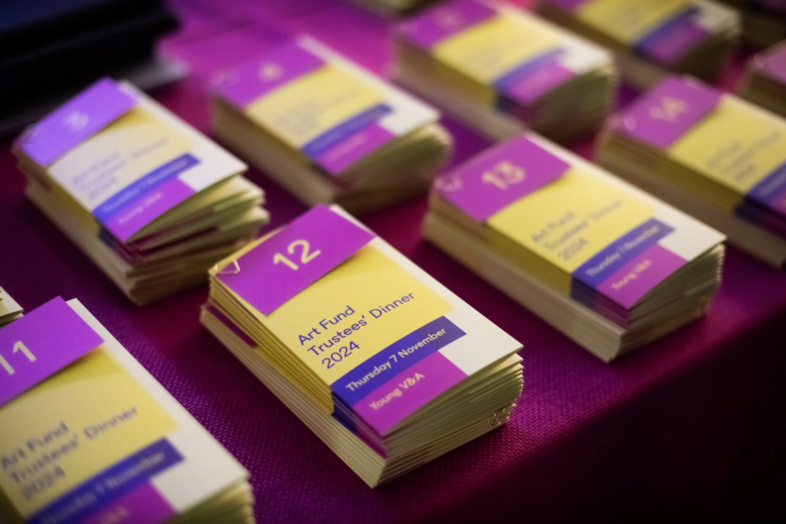 Stacks of yellow and purple event programs on a purple tablecloth at a fundraising event.