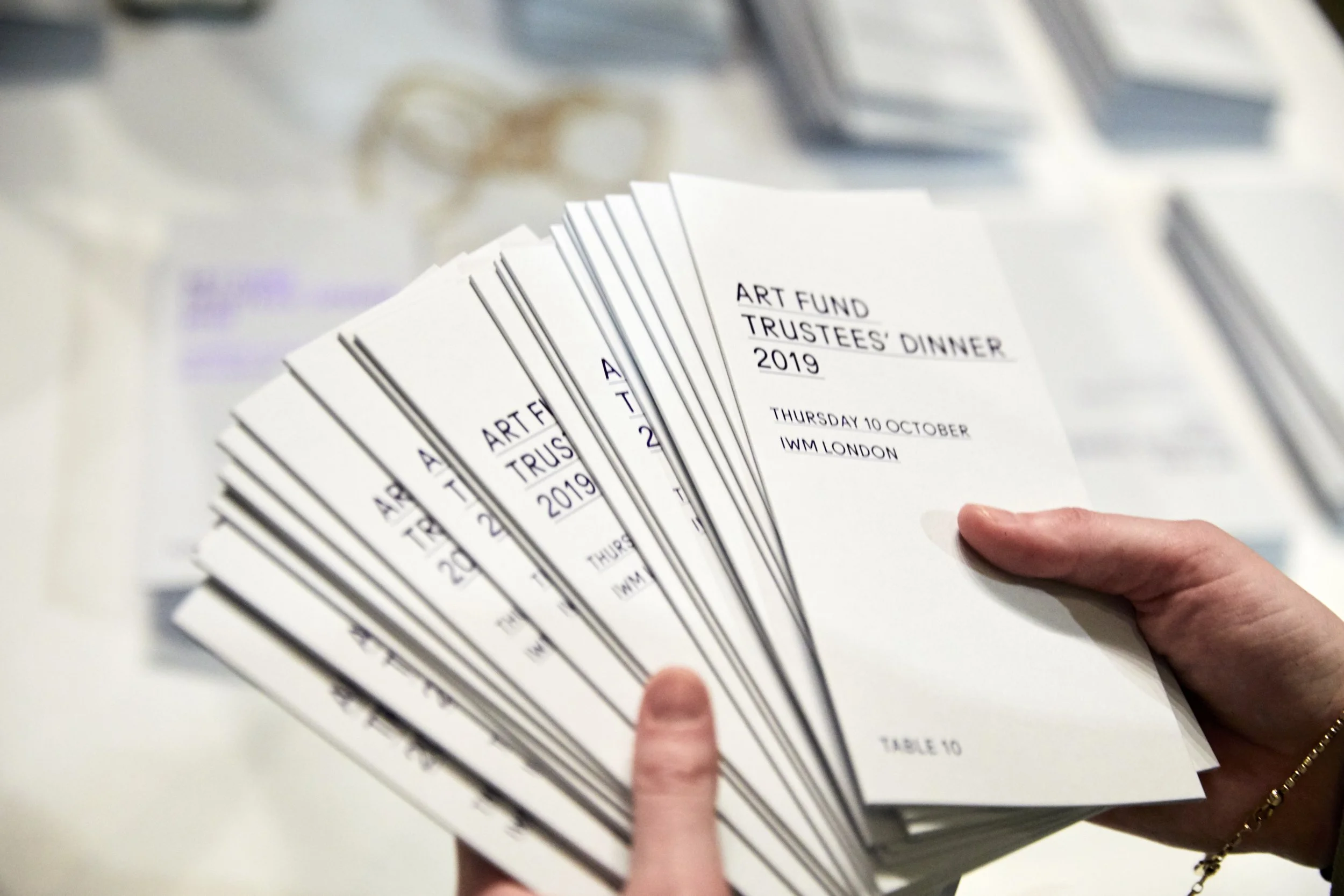 A person holding a stack of event tickets for the 2019 Art Fund Trustees' Dinner in London.