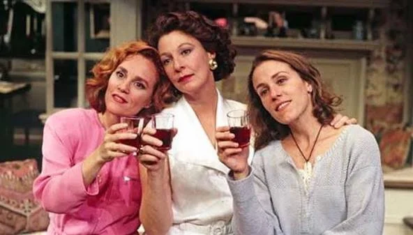 Three women holding glasses of red wine and smiling indoors.