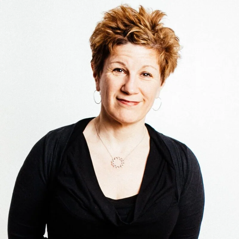 Portrait of a woman with short reddish hair wearing a black top and necklace, smiling at the camera.