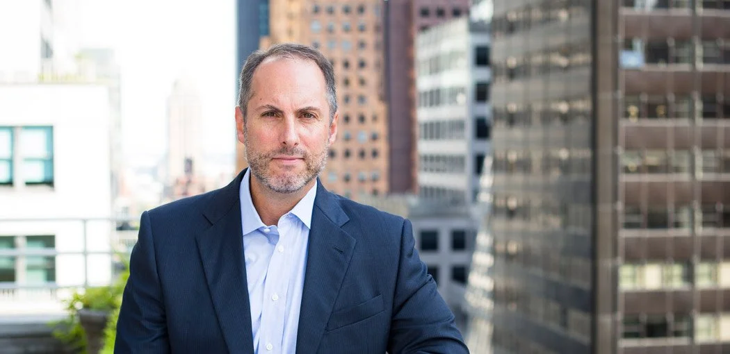Professional man in a suit standing outdoors on a city rooftop with skyscrapers in the background.
