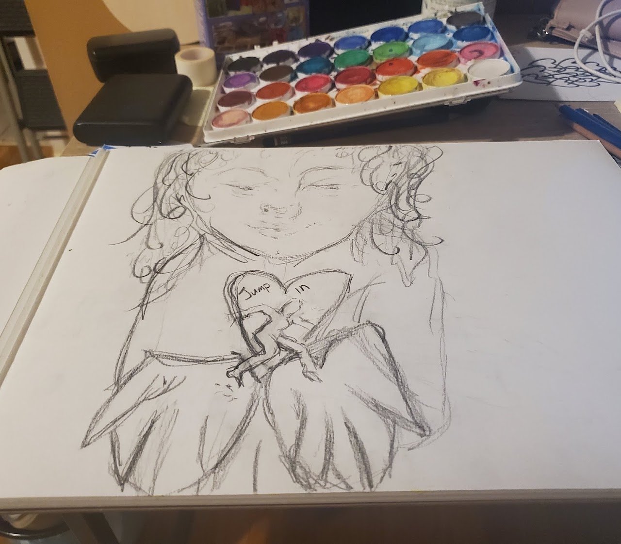 Sketch of a girl with curly hair holding a heart-shaped object with the words 'Jump in' written on it, on a desk with watercolor paint set and art supplies.