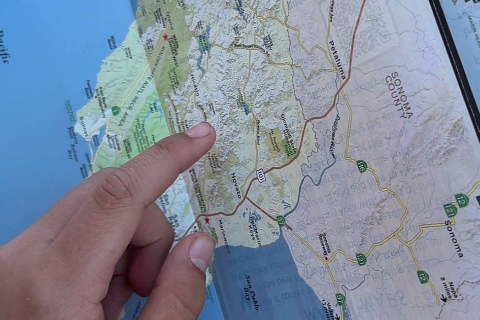 Close-up of a hand pointing at a regional map of the Pacific Northwest, showing Seattle and the surrounding areas with highlighted routes and landmarks.