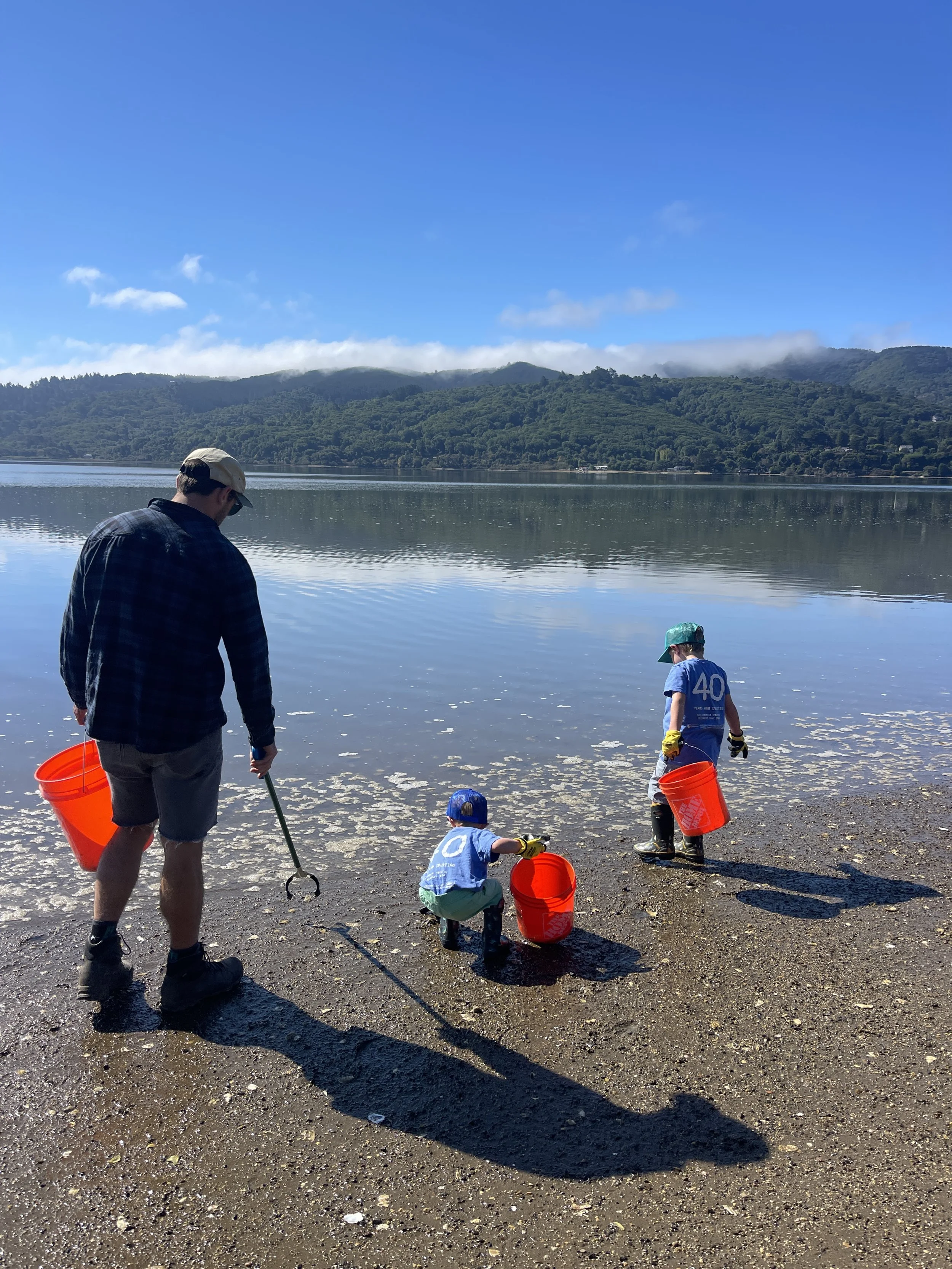 A man and three children with buckets by a lake, mountains in the background, on a clear sunny day.