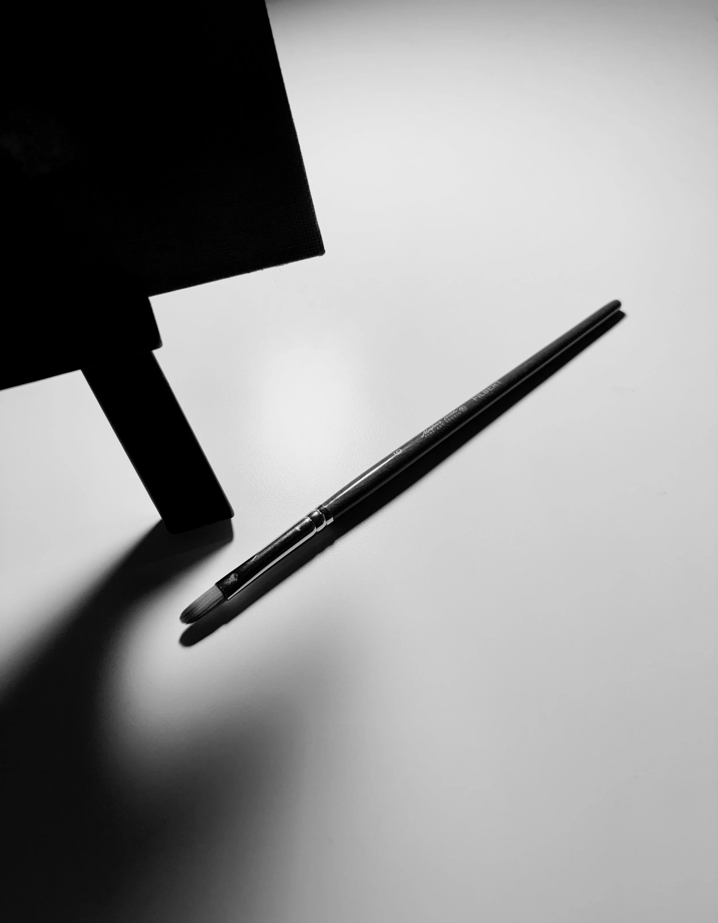 A black pen placed on a sheet of white paper with a shadow cast on its surface.