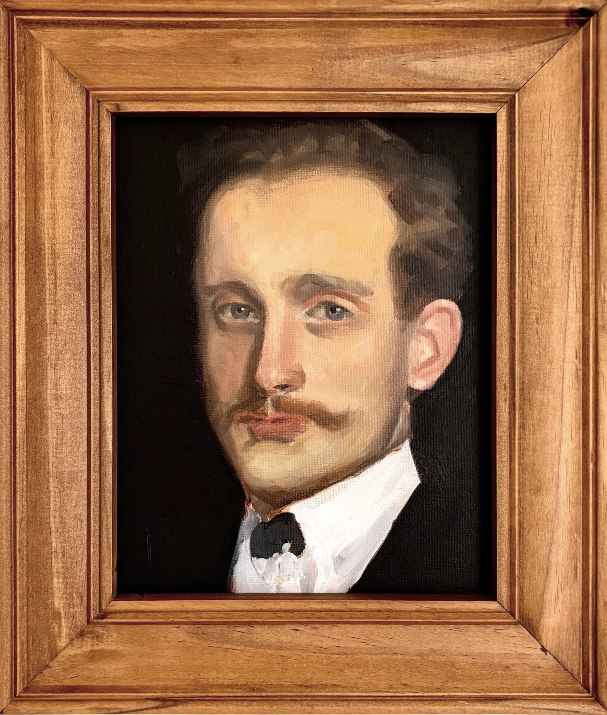 A framed portrait of a man dressed in formal attire with a white shirt and black jacket, featuring light skin, brown hair, and blue eyes, set against a dark background.