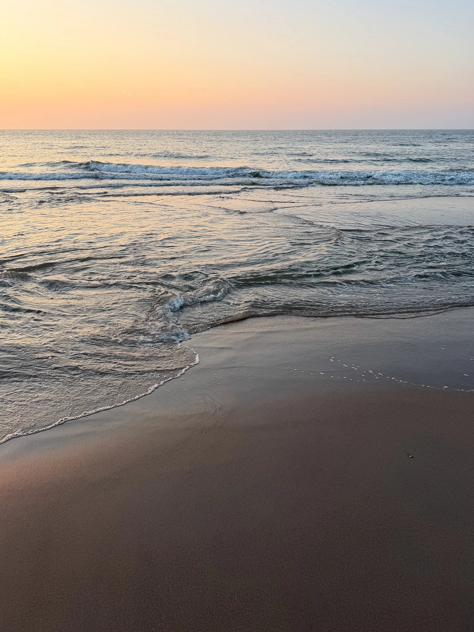 A beach scene at sunset with the ocean waves gently rolling onto the sandy shore under a pastel-colored sky.