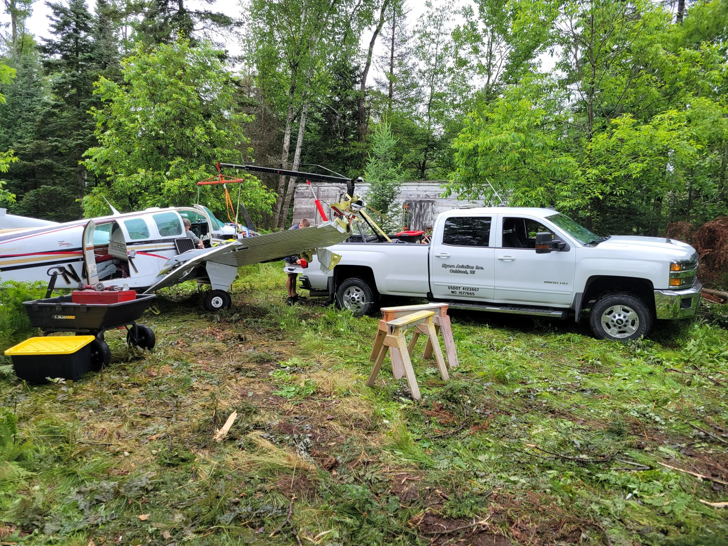 A small airplane has crashed into a pickup truck in a wooded area, with emergency equipment and personnel present at the scene.