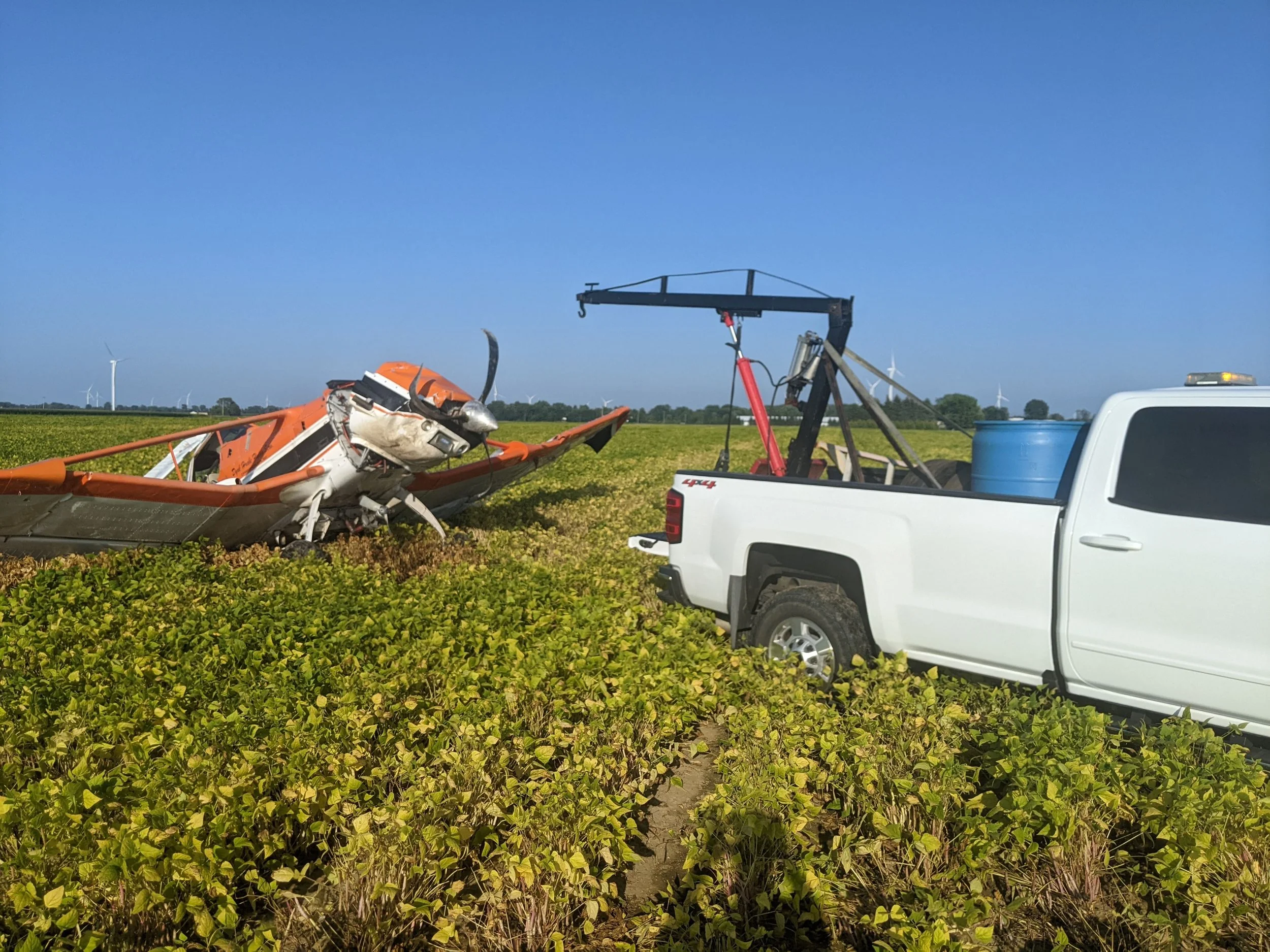 An orange small aircraft appears to have crashed in a field of green plants.