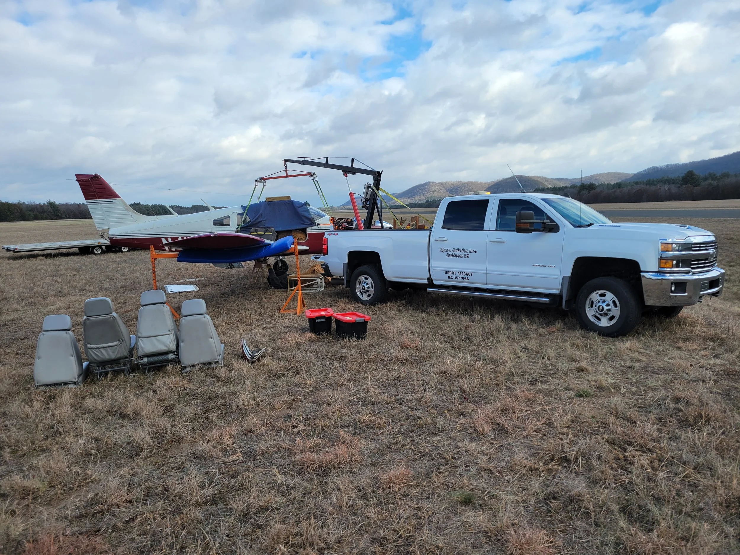 A white pickup truck parked in a field with a small private plane on a trailer attached to it.