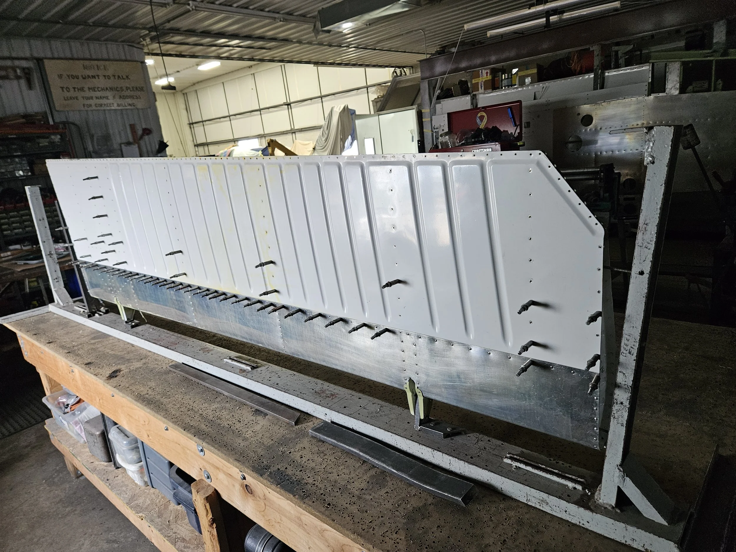 A workshop with metal and aluminum parts on a wooden workbench, tools, and equipment, in a garage or industrial setting.