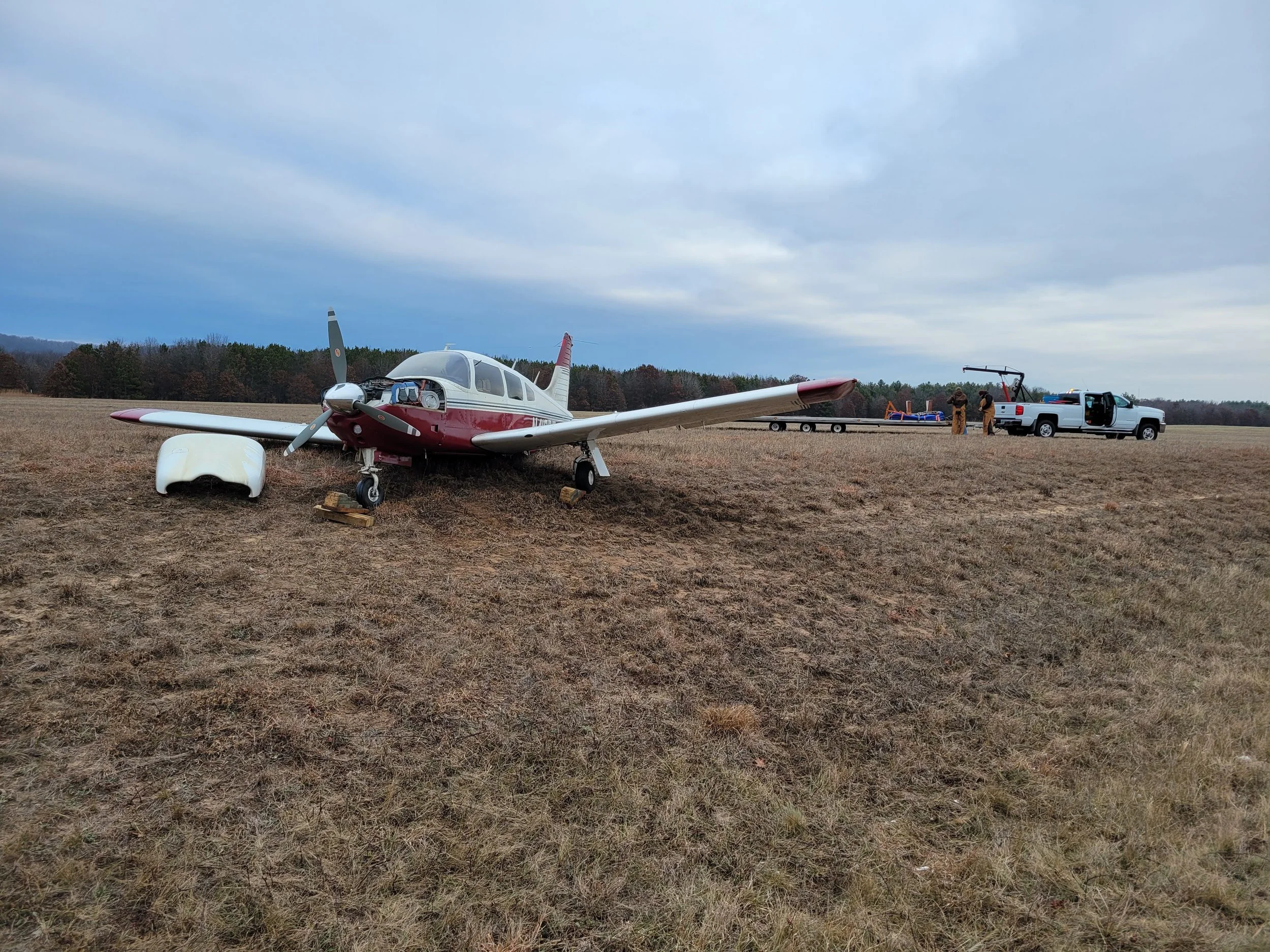 Small airplane on a grassy field with a pickup truck and two people near equipment in the background.