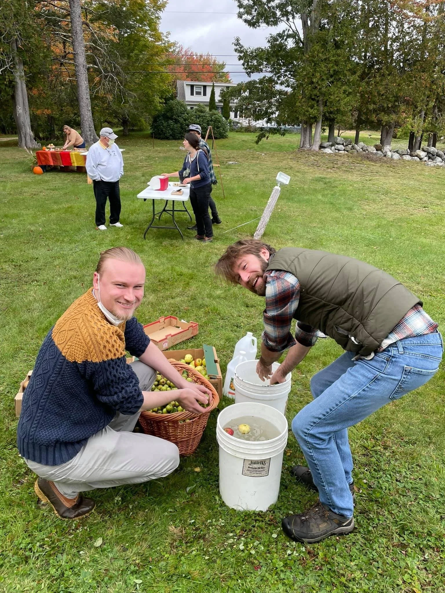 People gathering in a backyard during fall, harvesting and washing apples in preparation for juicing for cider.
