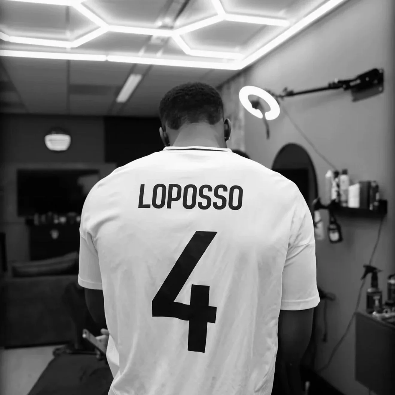 Zwart-wit foto van een man van achteren die een wit sportshirt draagt met de naam 'LOPOSSO' en het nummer 4.