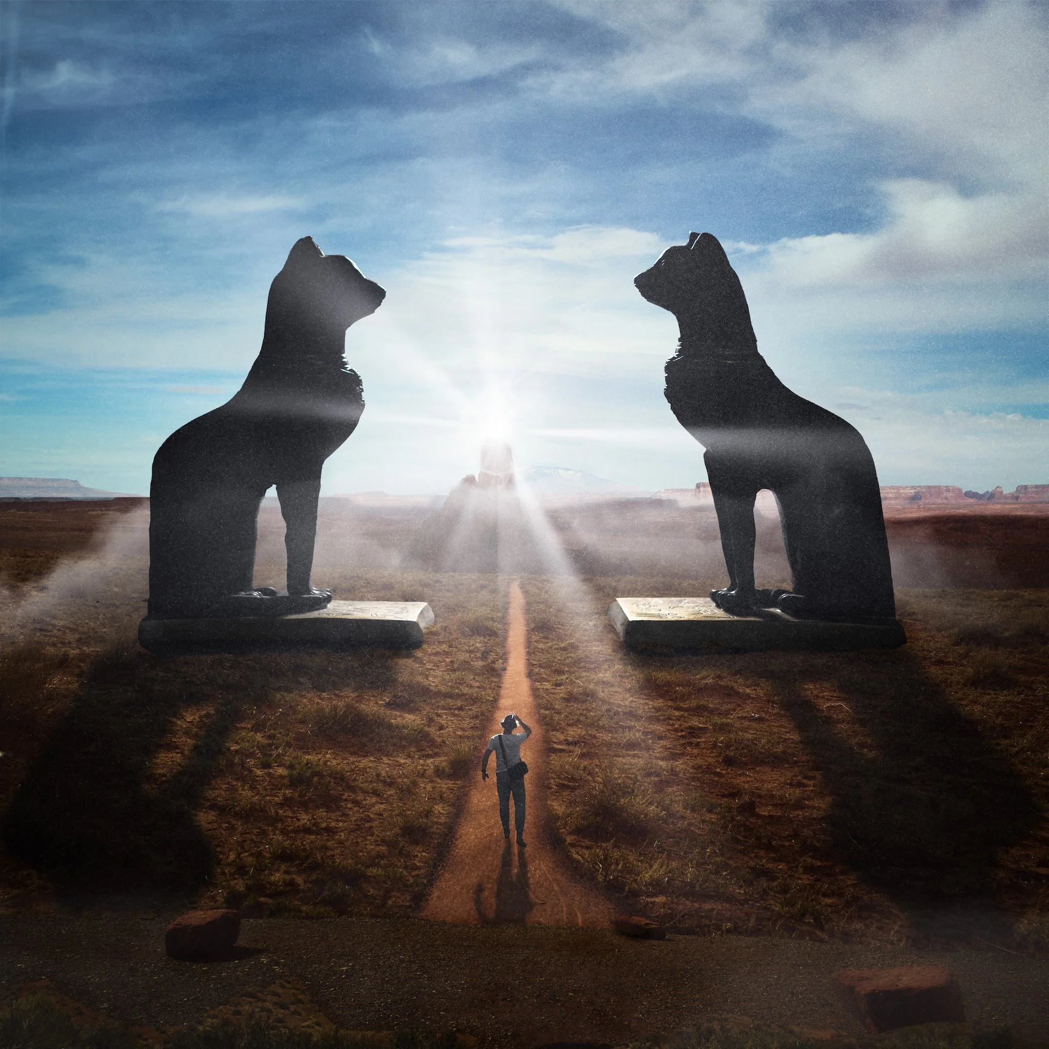 Two statues of dogs facing each other with a person standing between them, all appearing as silhouettes against a bright sky with clouds and landscape in the background.