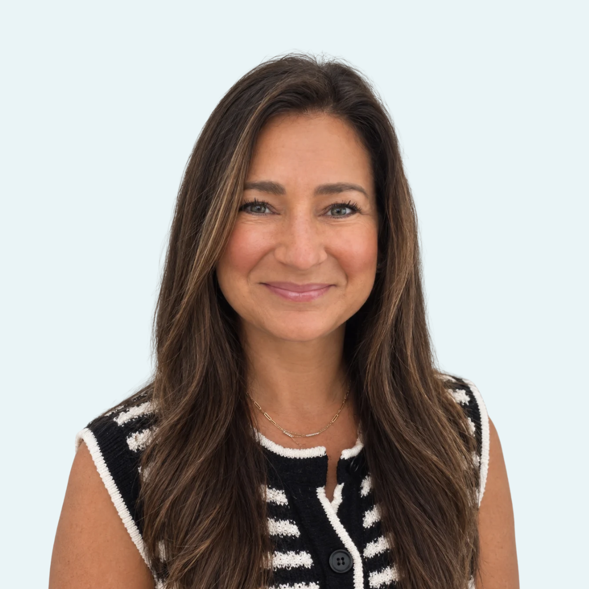 A woman with long brown hair smiling, wearing a black and white striped sleeveless top, against a light blue background.