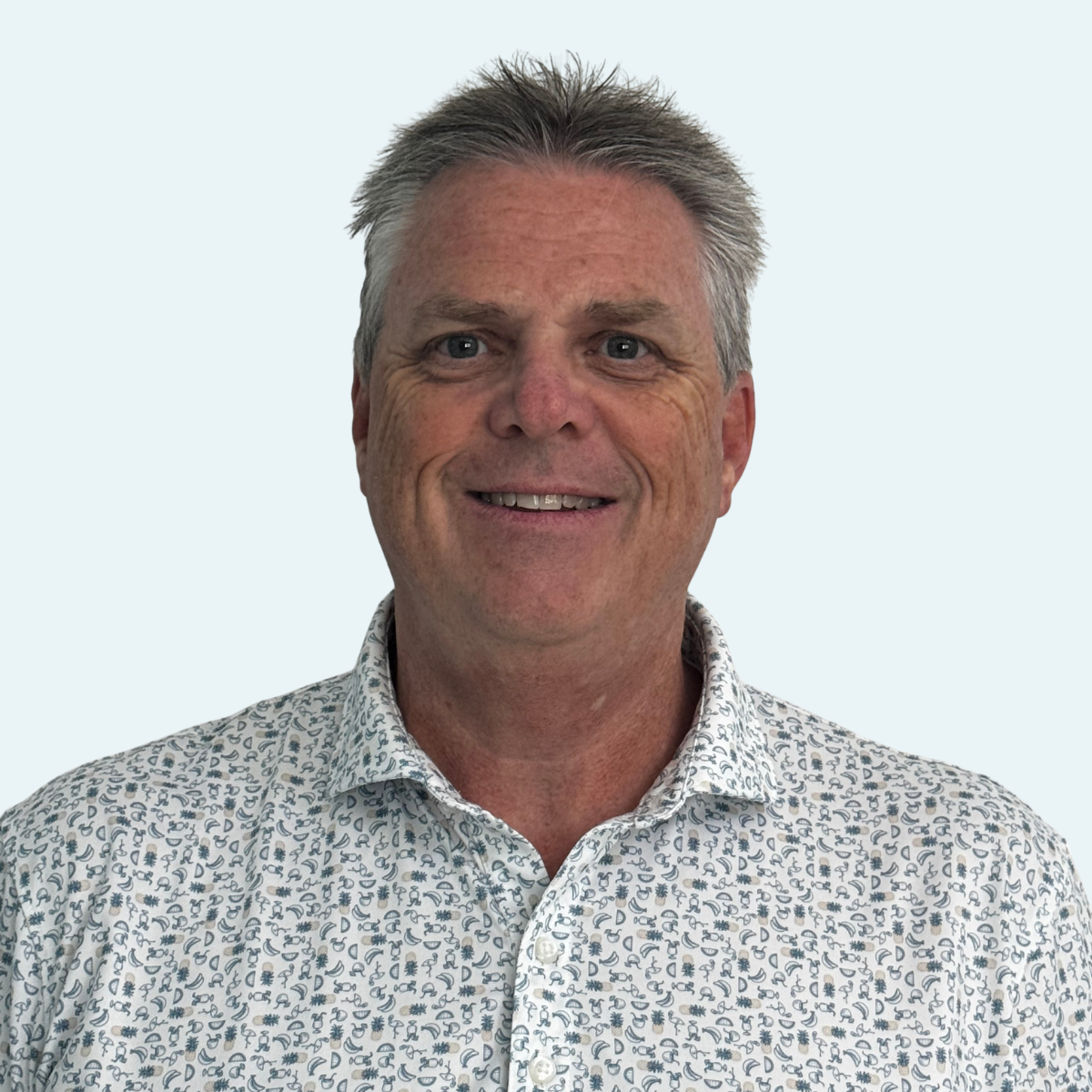 Portrait of a middle-aged man with gray hair, smiling, wearing a patterned button-up shirt, against a light background.