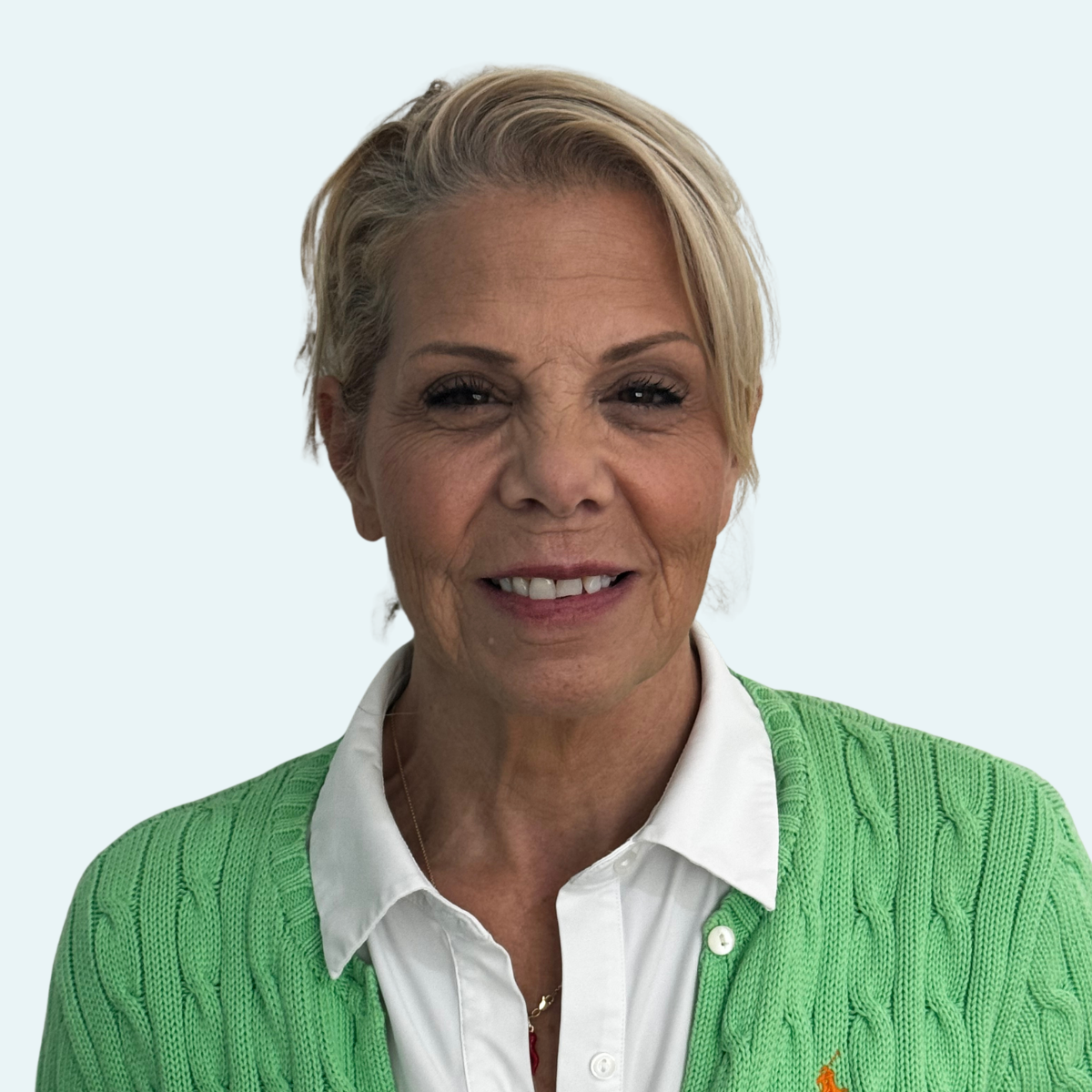 A smiling woman with short blonde hair wearing a white collared shirt and a green sweater.