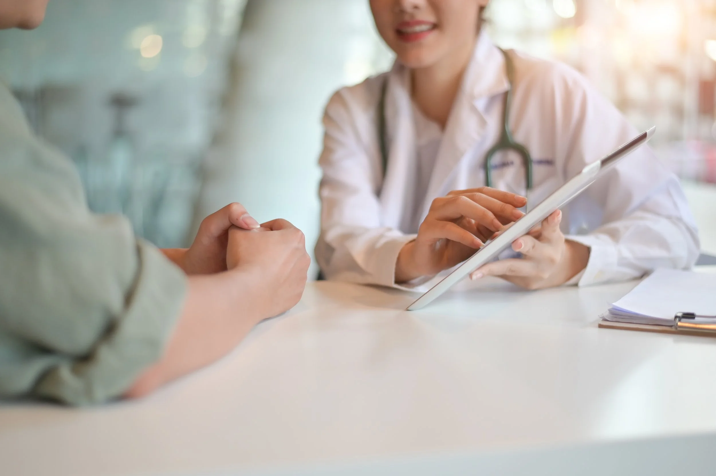 Healthcare professional, possibly a doctor, showing a tablet to a patient in a clinical setting.