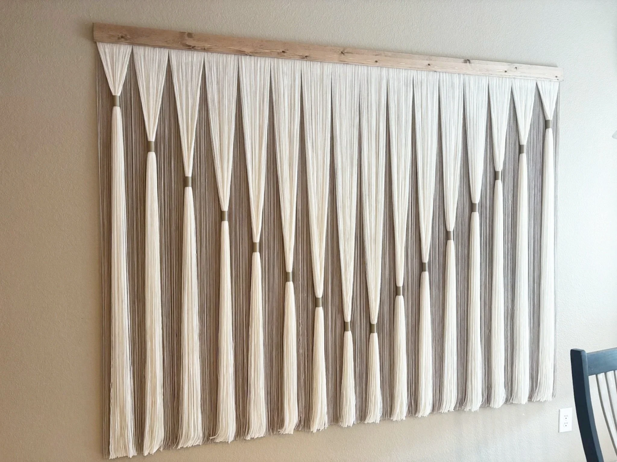 A decorative wall hanging made of white pleated strips arranged vertically on a wooden frame.