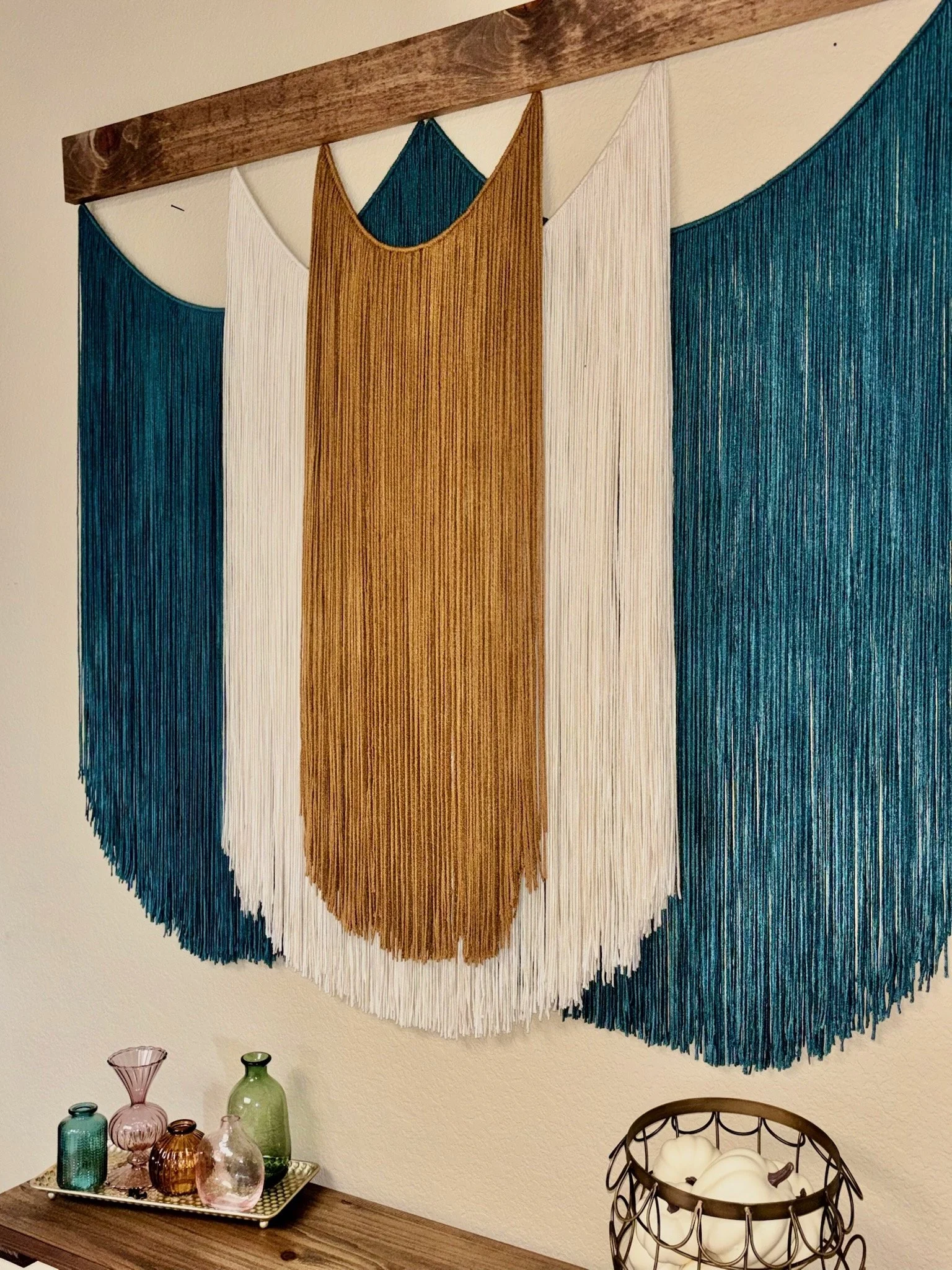 A wall hanging made of vertical strings in blue, white, and tan colors, creating a geometric pattern.