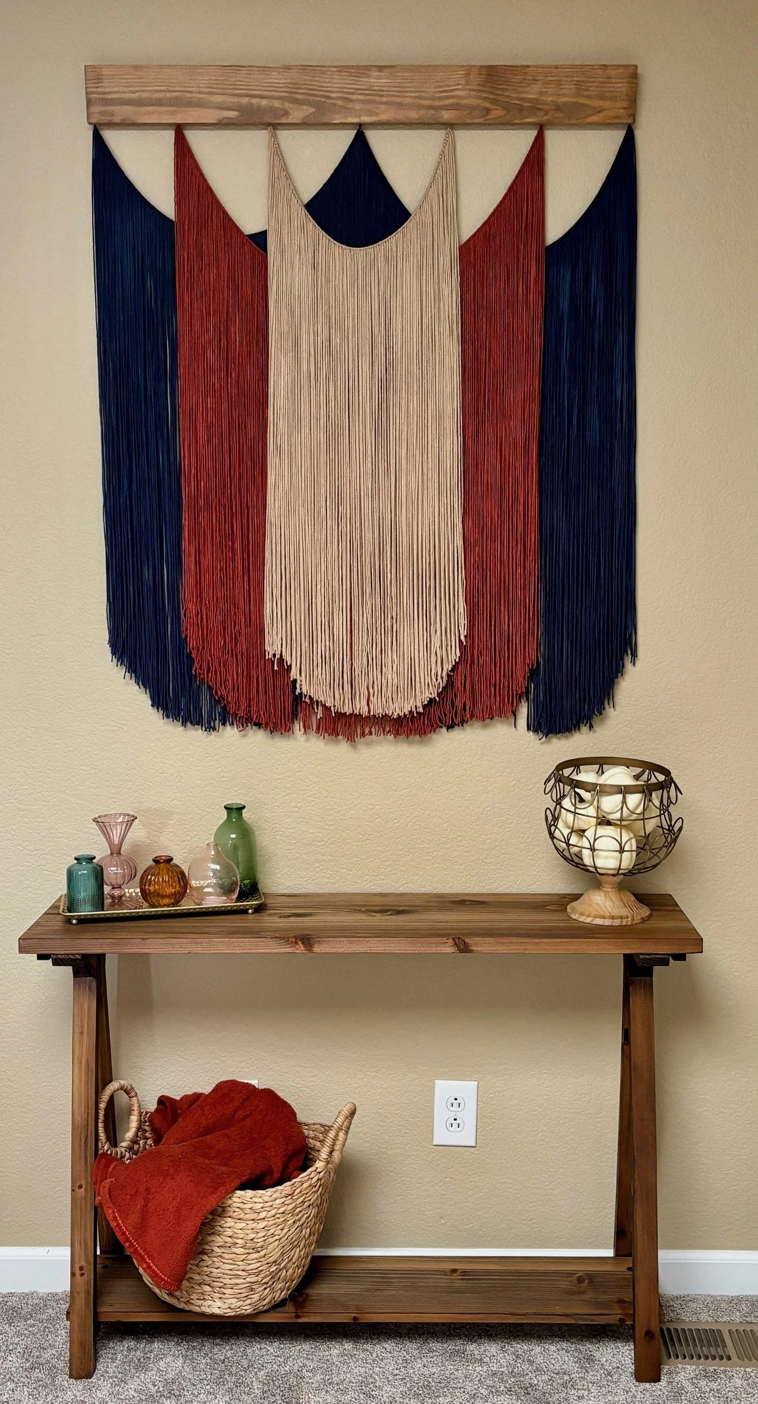 Vale custom yarn wall hanging featuring layered navy, rust and neutral yarn suspended from a handcrafted wooden base.