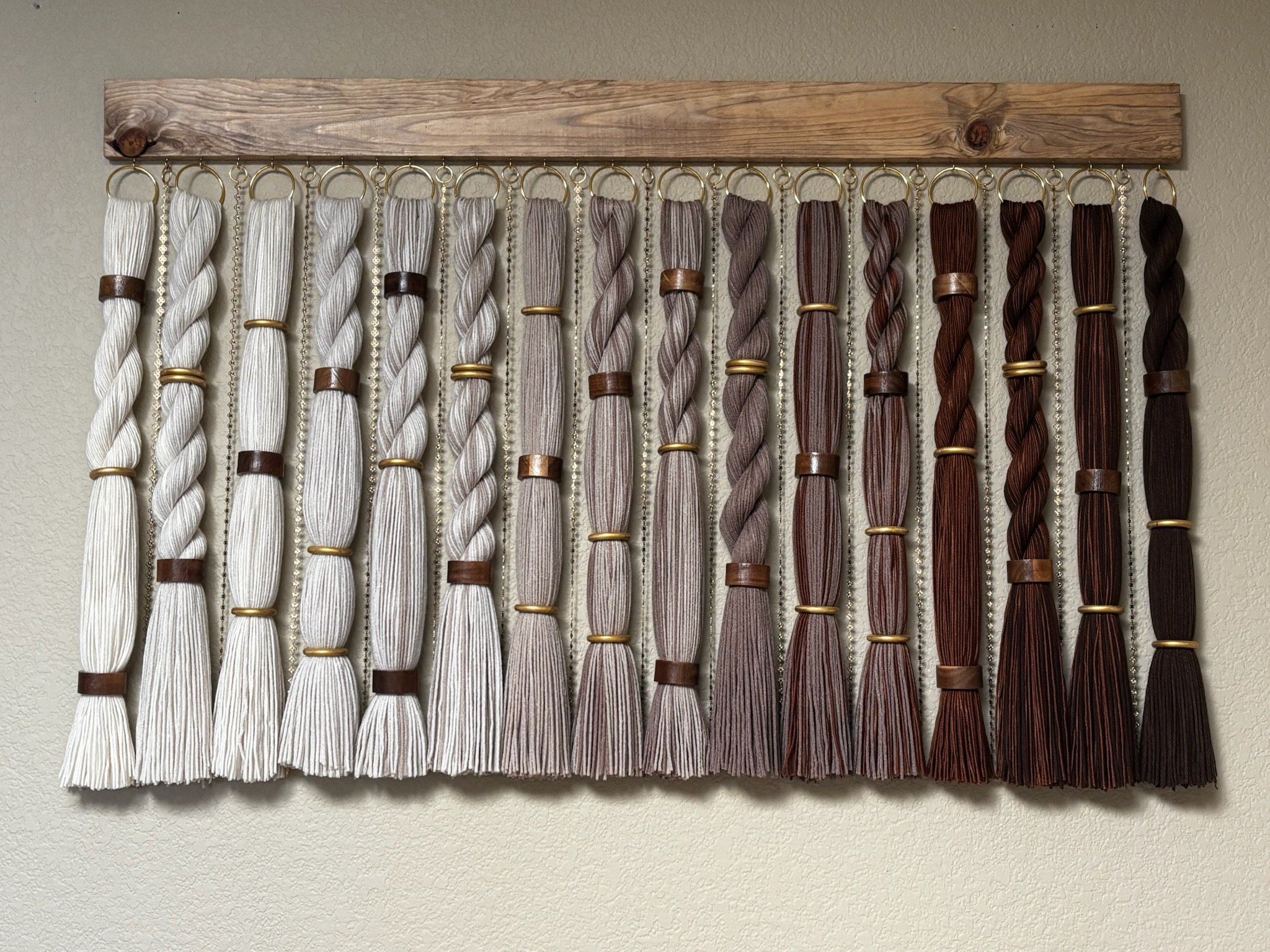 Display of multiple embroidery floss skeins hanging on a wooden rack against a beige wall.