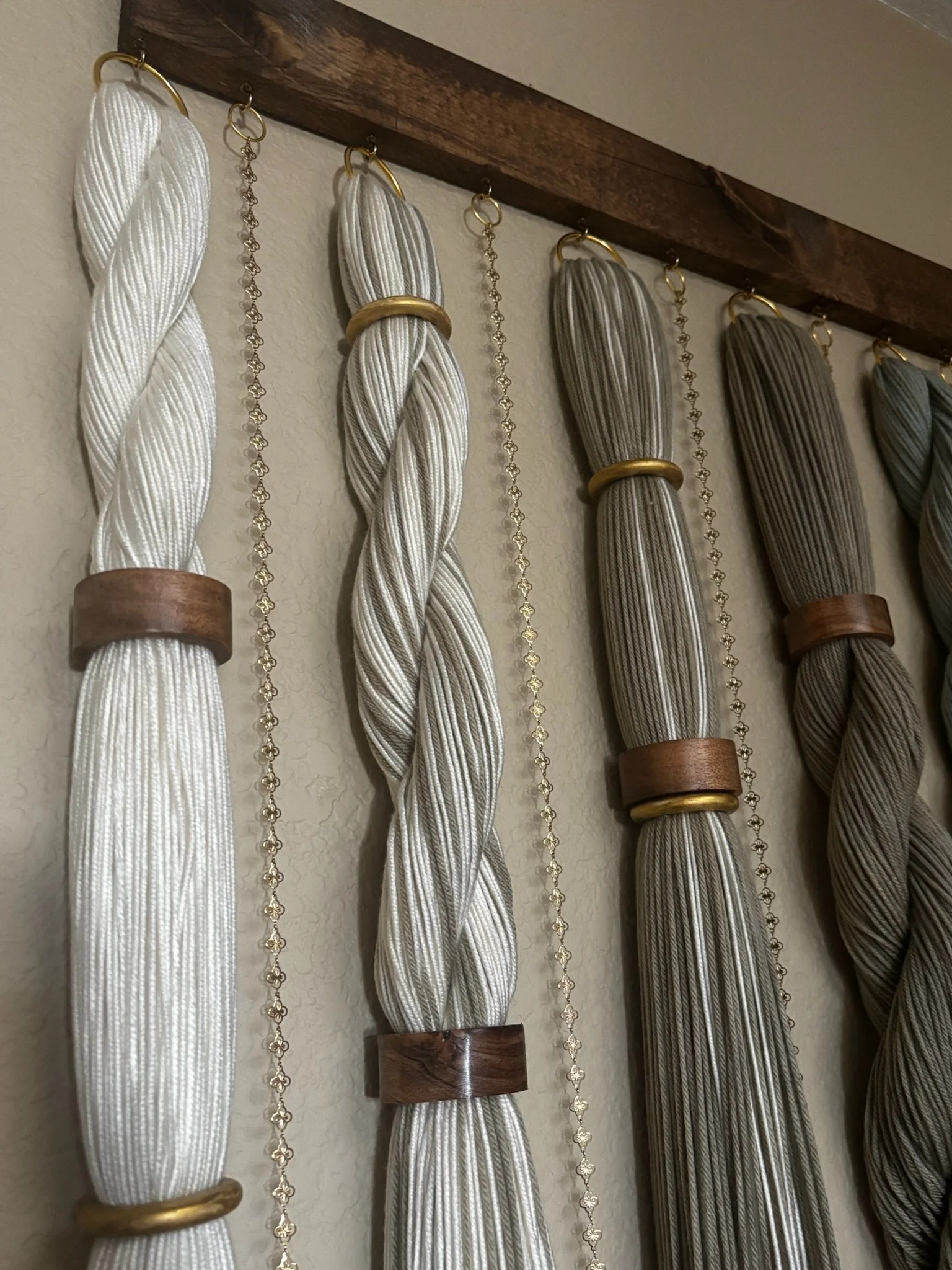 Decorative curtain tiebacks made of twisted white and gray cords with gold rings and chains, mounted on wooden wall brackets.