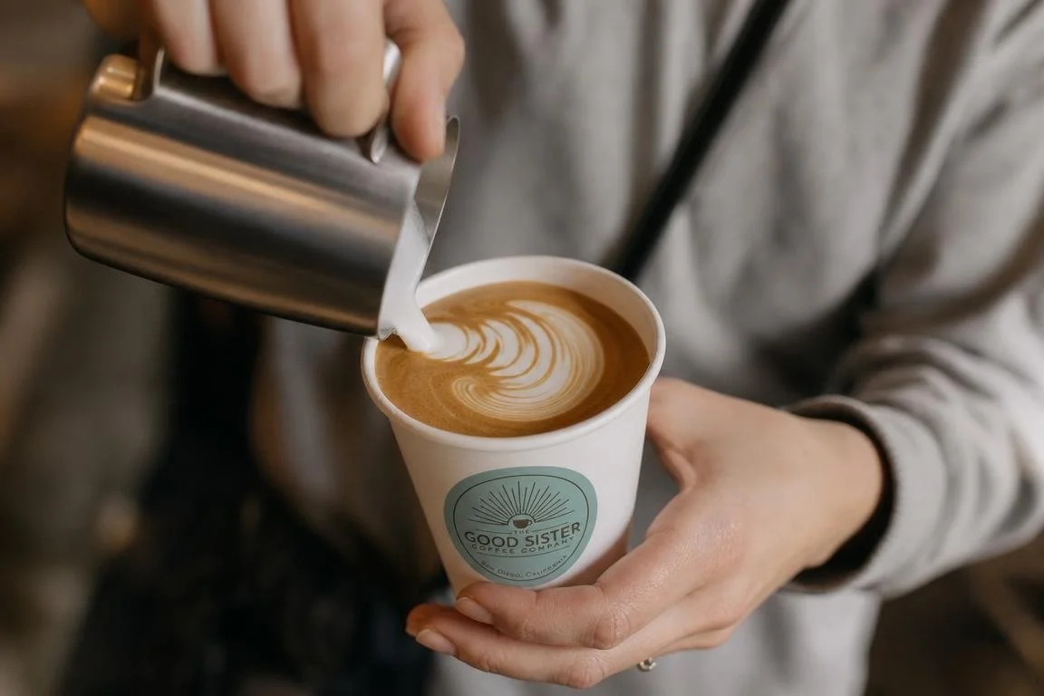 Person pouring steamed milk into a cup of coffee to create latte art at a cafe.