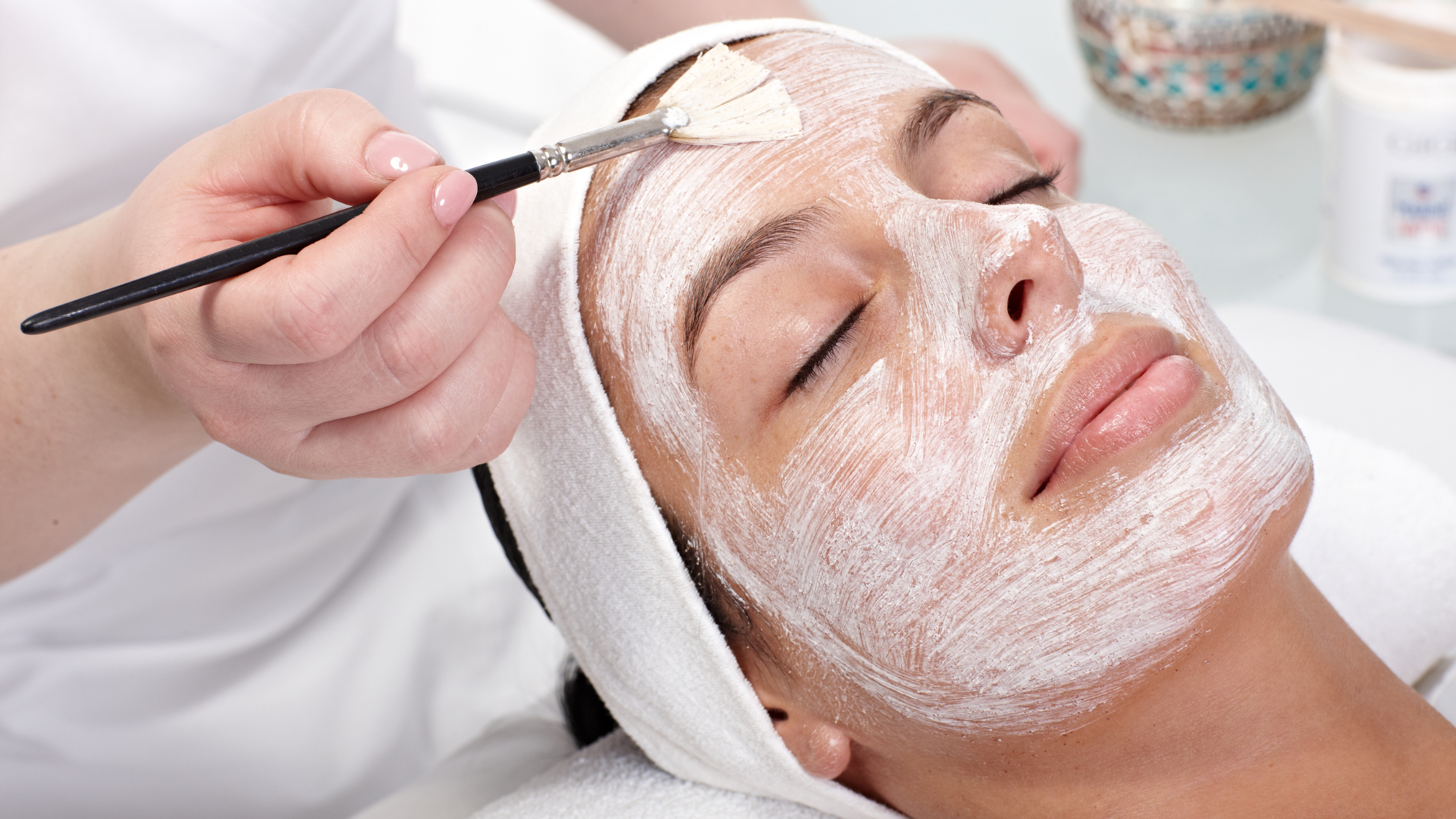 A person is lying down with a facial mask applied, receiving a facial treatment in a spa or clinic setting.