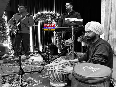 Musicians performing on stage, including a sitar player, a guitarist, and a keyboardist, with a news channel logo in the background.