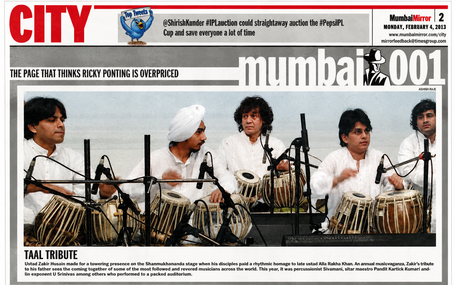 Band of musicians playing traditional Indian drums called tabla during a tribute performance at an outdoor event. They are dressed in white, with one musician wearing a turban, and are seated behind microphones with a sky in the background.