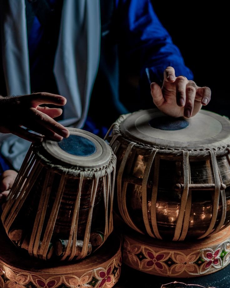 Person playing the tabla, an Indian musical instrument, with hands on the drums.