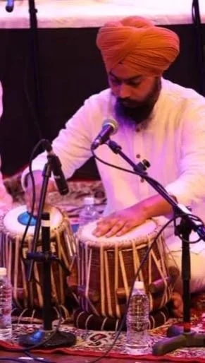 A man wearing a turban playing tabla drums during a performance or recording session, with microphones and water bottles around him.