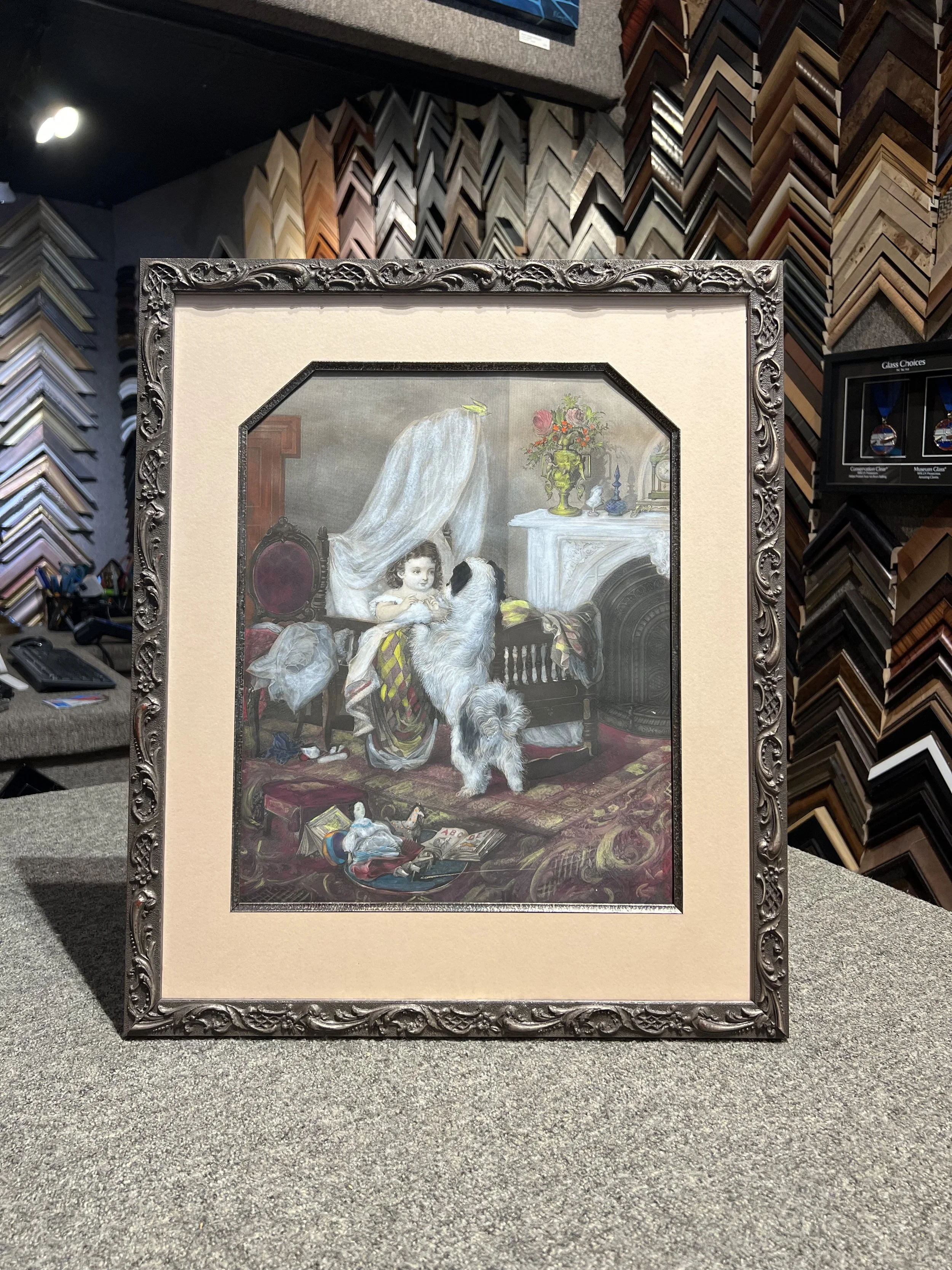Framed painting of a young girl with a dog in an elegant room with flowers and decorative objects.