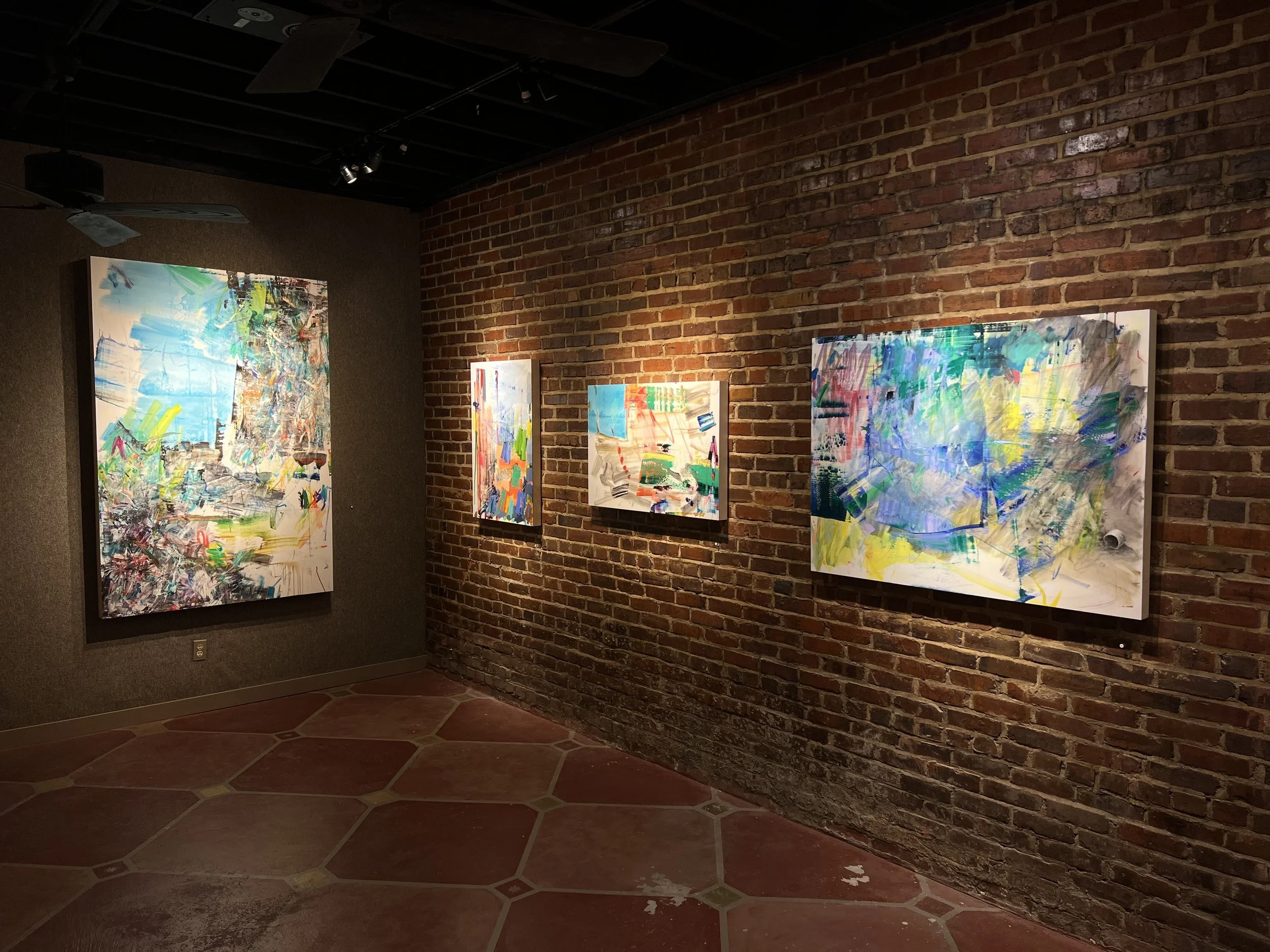 Abstract colorful paintings displayed on a brick wall in an art gallery.