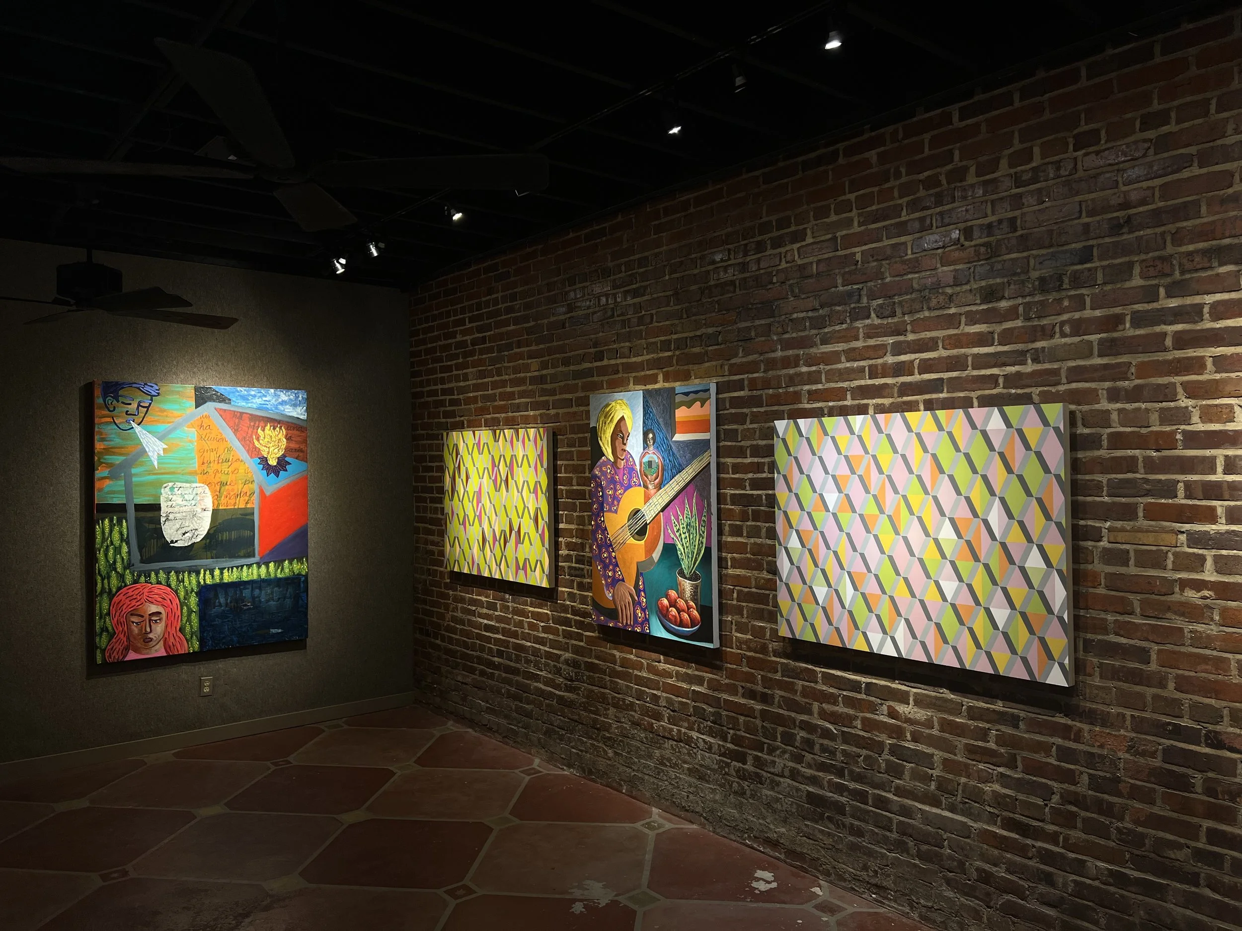 An art gallery with a brick wall and modern paintings. The paintings depict various colorful, abstract, and figurative art with human portraits, geometric patterns, and lively scenes.