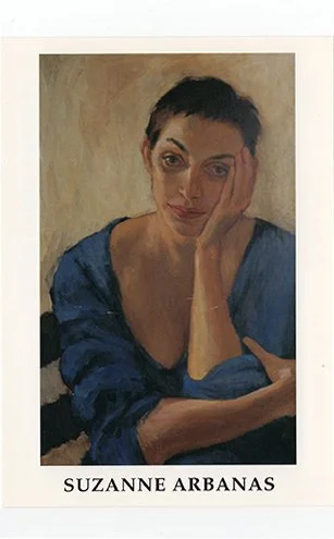 A portrait of a woman with short dark hair, wearing a blue top, resting her face on her hand, with a neutral background.