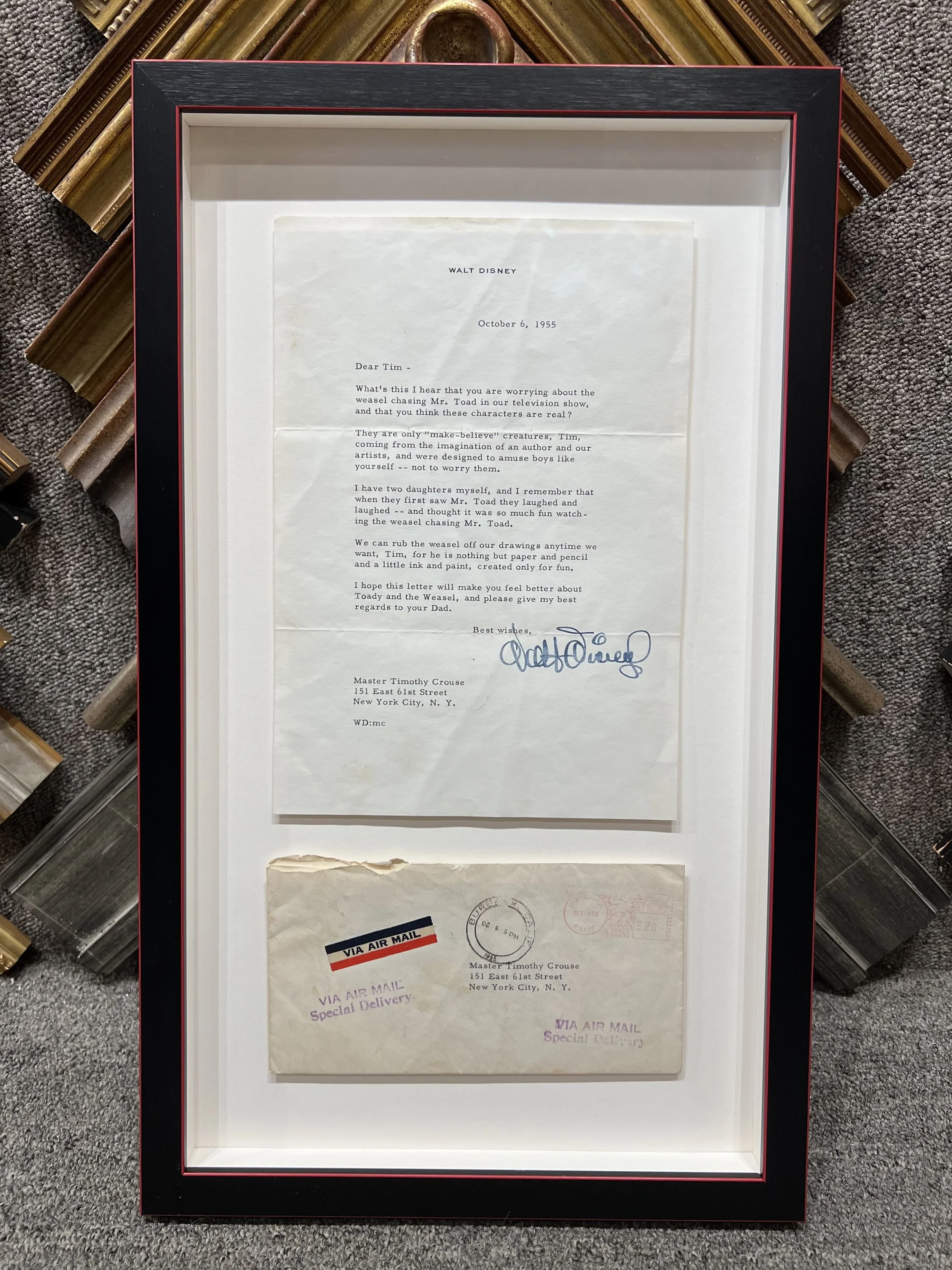 A framed letter with the date October 6, 1955, addressed to Tim from Walt Disney, discussing the character Mr. Toad and a drawing of him, signed by Walt Disney. The frame contains a letter and some official mail envelopes behind it.