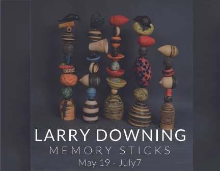 A collection of memory sticks from Larry Downing displayed in vertical stacks with labels noting the exhibit dates from May 19 to July 7.